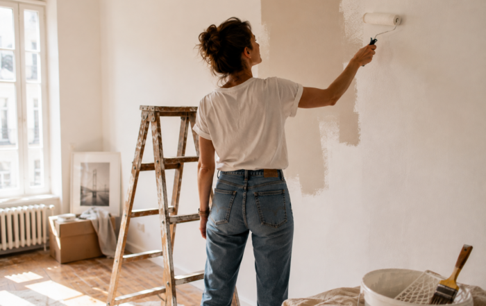 Frau tapeziert eine Wand in ihrem Zuhause und setzt den ersten Schritt einer Veränderung um – Sinnbild dafür, das eigene Leben aktiv zu gestalten und nicht länger nur zuzusehen.